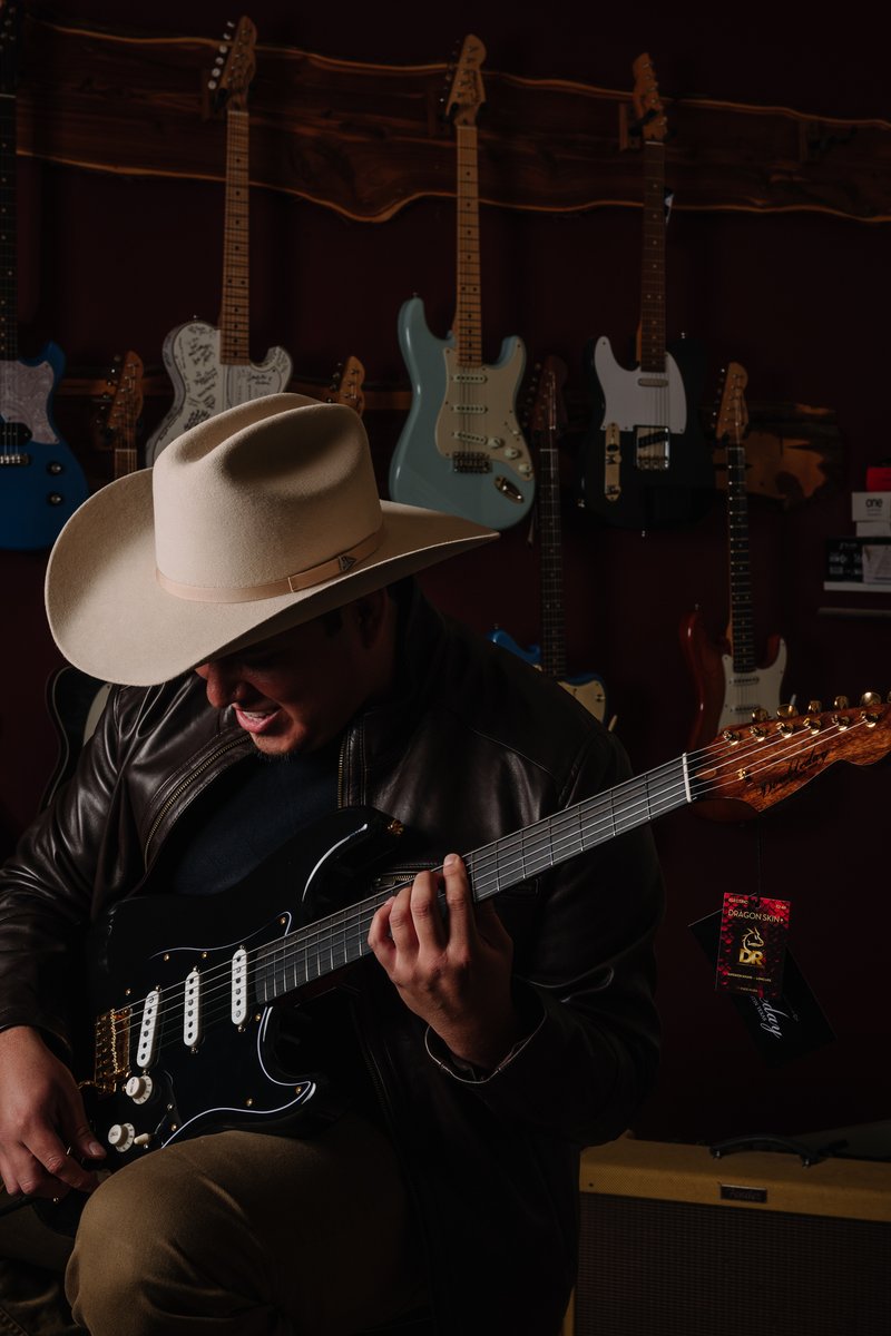 Jason Cuellar with guitar, in front of the guitar wall